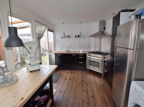 Open moderne L-vormige keuken met apparatuur zoals een RVS- gaskookplaat, oven, koelkast en afzuigkap.