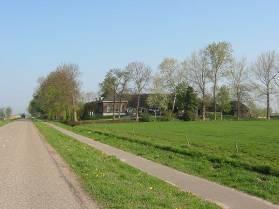 met solitaire bomen aan de voorzijde, een hooiberg achter en een boomgaard opzij, omsloten door een groensingel.