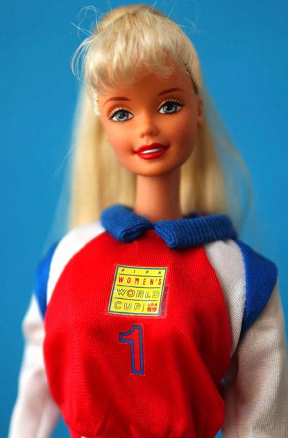Soccer Barbie heeft haar lange, blonde haren van achter in een paardenstaart gebonden, met een pony op haar voorhoofd.