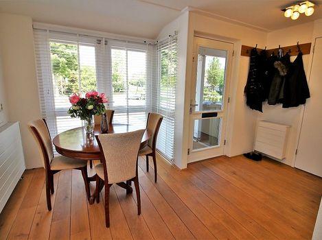 Vanuit de keuken kijkt u de riante woonkamer in. De woonkamer is lager gelegen en is voorzien van een prachtige massief houten vloer en een gevelbrede glazen pui met schitterend uitzicht.