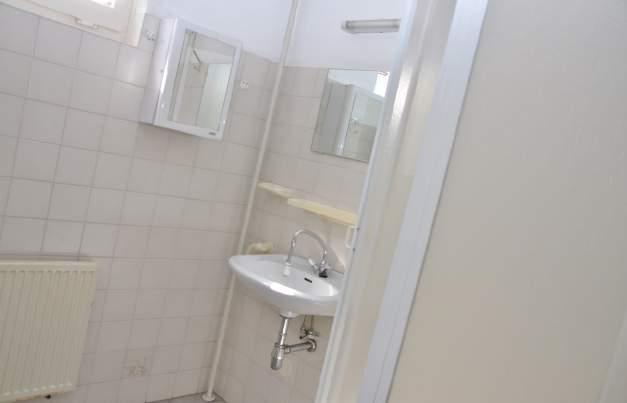 Geheel betegelde badkamer met vaste wastafel, toilet, douche en