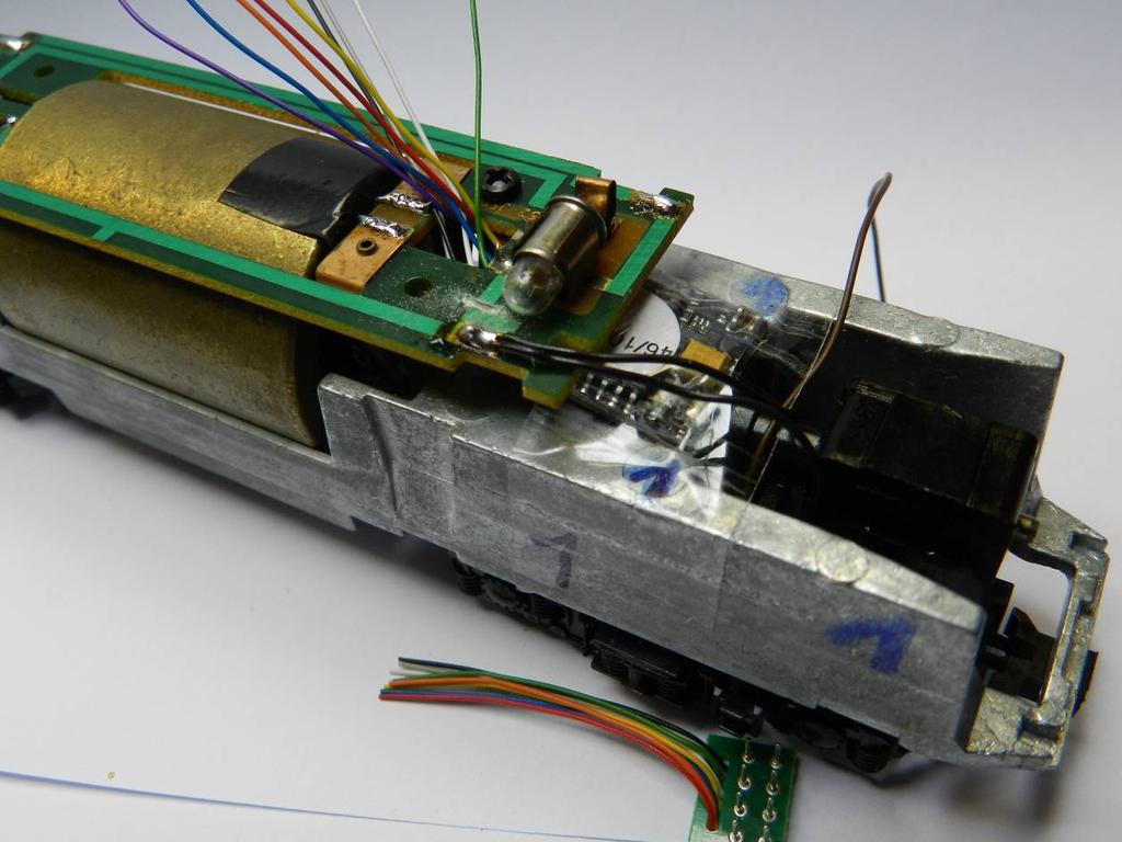 Plaats de decoder (het NEM-plaatje hebben we eraf geknipt zodat de draden makkelijk kunnen gesoldeerd worden) en voer de draden door het gat in de platine waar vroeger de diodes aan de motor zaten.