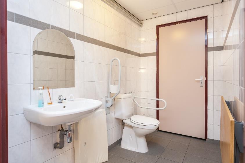 Geheel betegeld invalidentoilet met toilet en vaste wastafel.