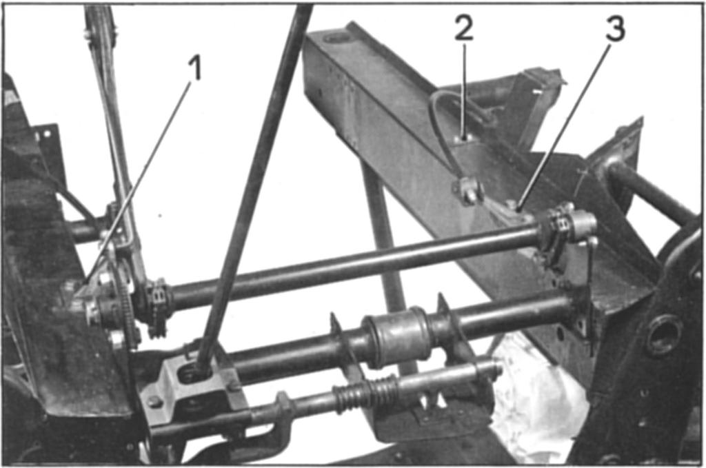 14 34. Montage van de achterste traverse/motorsteun a) Schuif de traverse tezamen met de handremhefboom en -kabels tussen de langsliggers.