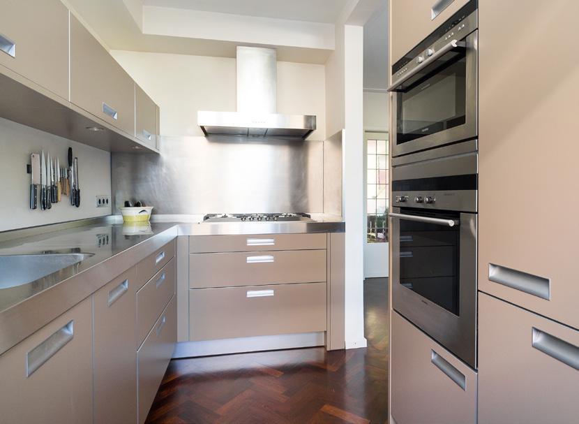 Luxe open keuken met een modern keukenmeubel in hoekopstelling met een RVS werkblad en apparaten-/ kastenwand.