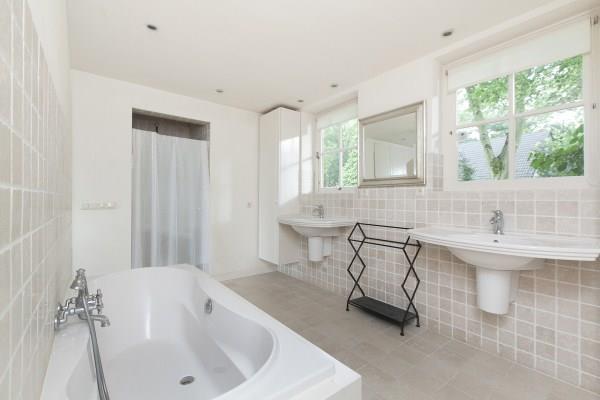 De luxe badkamer is deels betegeld met getrommeld marmer en uitgerust met een ligbad, 2 vaste wastafels met een bergmeubel, een separate douche en